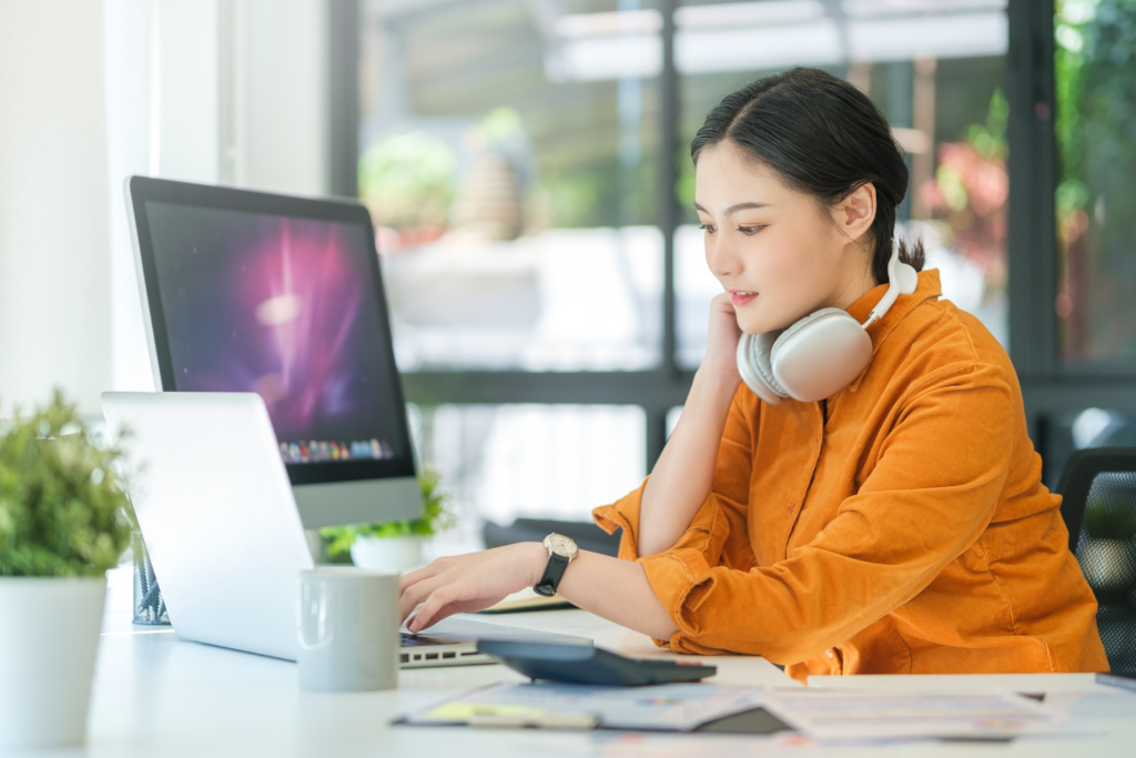 MacとWindowsで首にヘッドフォンを掛けて、動画編集をしている若い女性